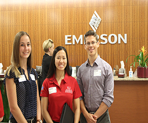 Fellows Brooke Reid, Annie Lynn, and Ethan Zolotor pose in front of the Emerson logo during a visit to the company as part of SELF on the Road.