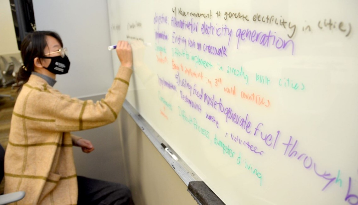A student working at a whiteboard at IHAWKe-a-THON