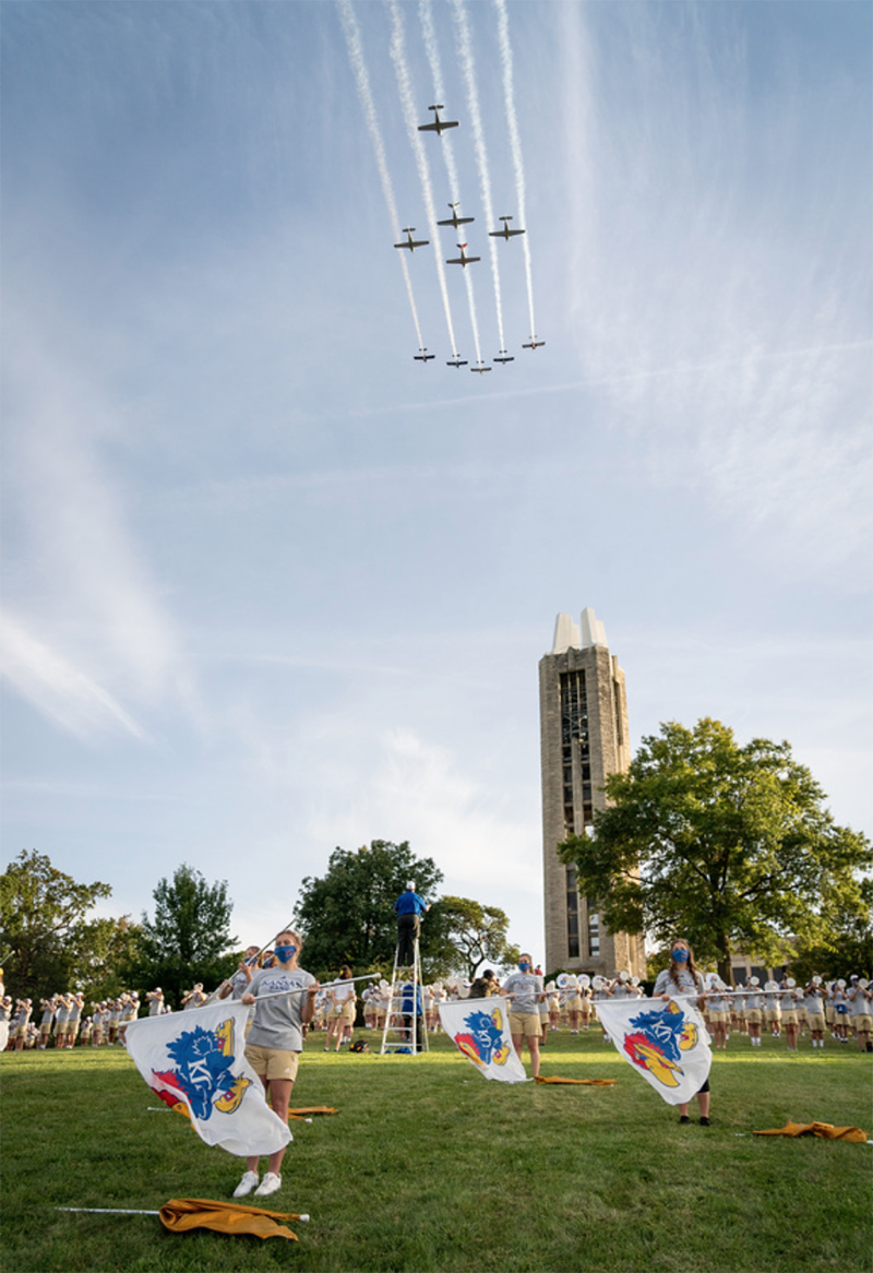 A KU Marching Band performance on the Campanile lawn with jets flying overhead