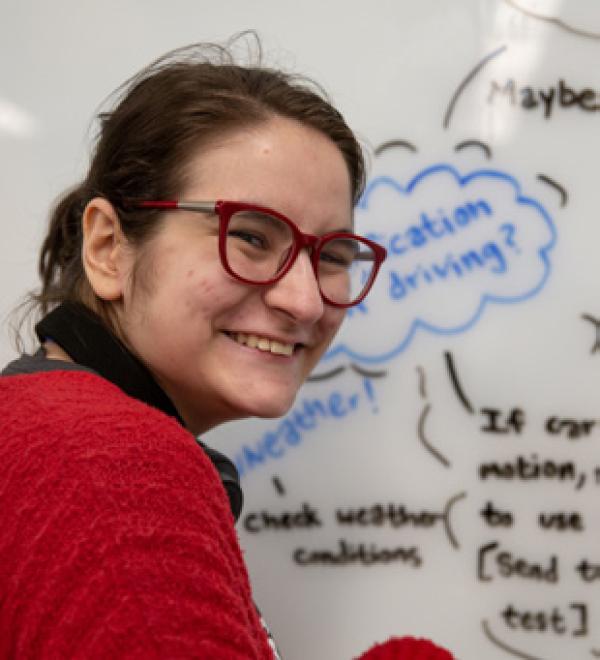 a student smiling in front of a whiteboard with writing